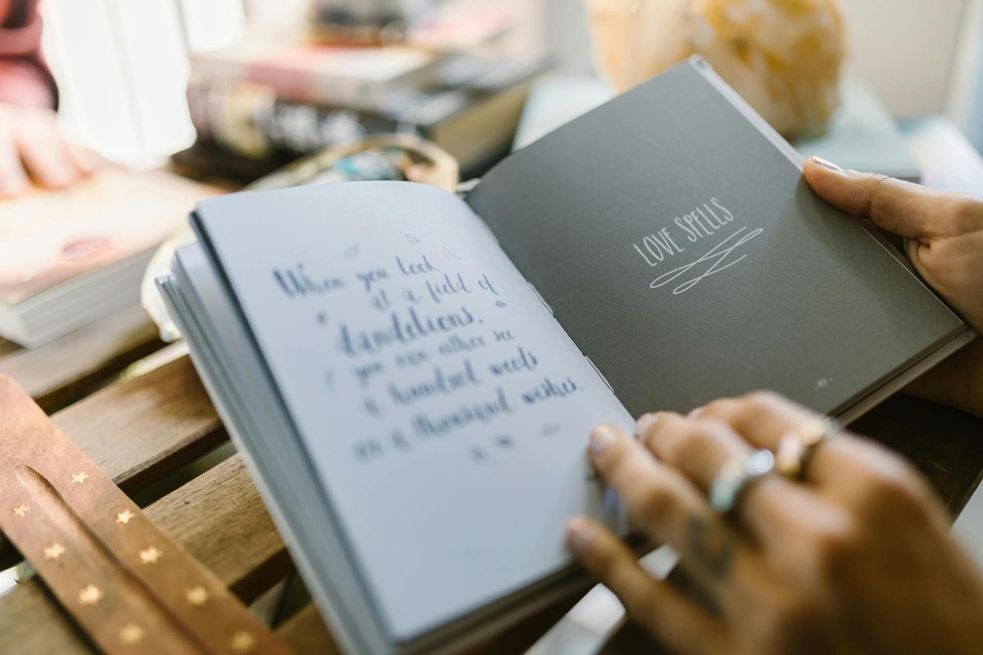 Close-up of hands holding an open book with text about love spells on a wooden table.